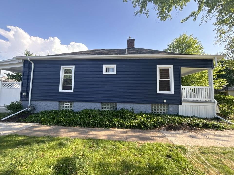 Single-story ranch home with fresh navy blue lap siding, white window trim, painted stone foundation, and a white porch railing
