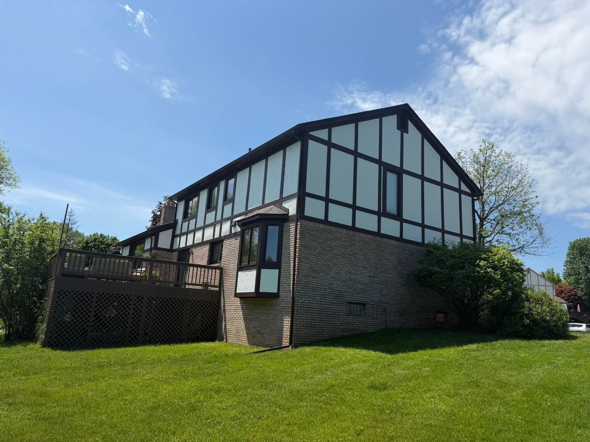 Two-story Tudor-style home with repainted light stucco panels, dark brown timber trim, and lower brick wall