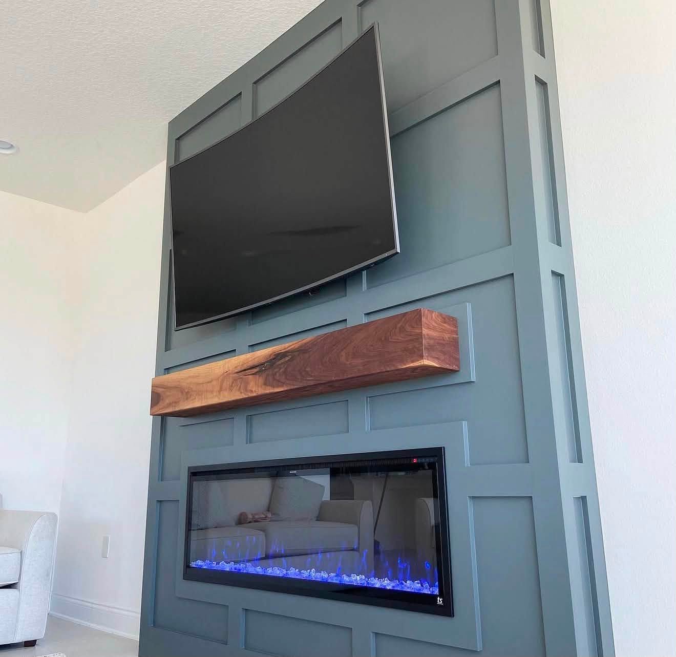 Interior accent wall with slate blue-green board-and-batten millwork, a live-edge walnut floating mantel, linear electric fireplace, and mounted TV