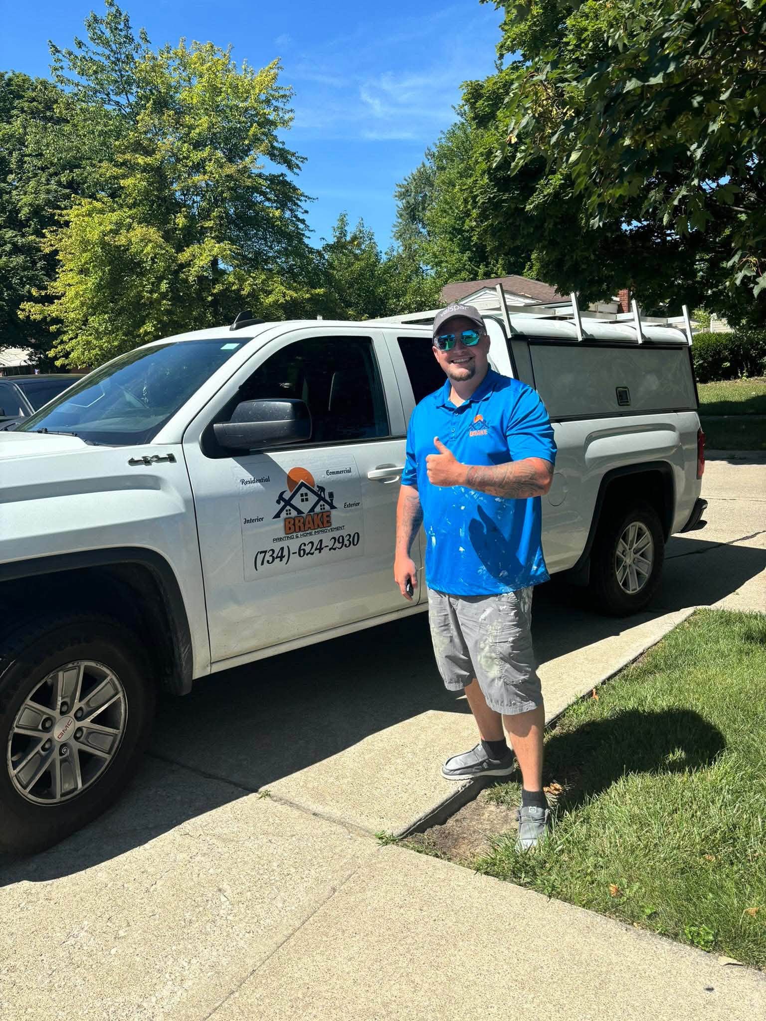 Jerry, owner of Brake Painting, in a blue company polo giving a thumbs up beside the branded work truck