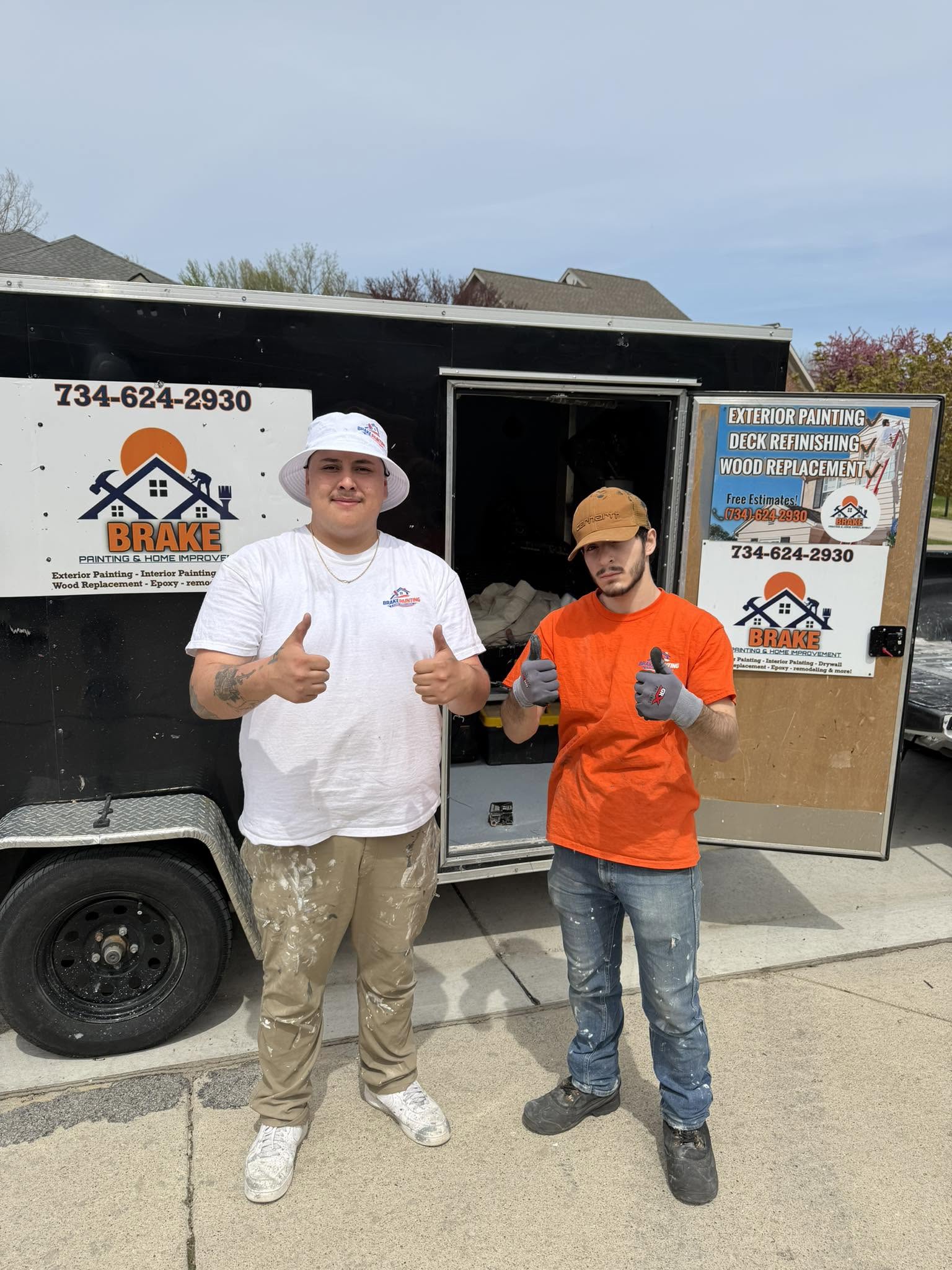 Brake crew members Miguel and Anthony giving thumbs up in front of the black Brake Painting work trailer
